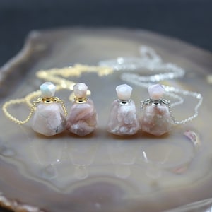 Op de afbeelding: Drie kettingen met parfumflesjes van roze agaat met gouden en zilveren kettingen. De flesjes hebben een gefacetteerde, geometrische vorm en zijn voorzien van een gouden of zilveren dop.