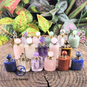 May include: A collection of small, rectangular perfume bottles carved from various gemstones, including rose quartz, amethyst, lapis lazuli, and tiger's eye. Each bottle features a gold-tone metal cap with a small, round gemstone topper.