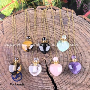 Puede incluir: Una colección de collares con colgantes en forma de corazón y cadenas doradas. Los colgantes están hechos de diversas piedras preciosas, incluyendo ojo de tigre, ónix negro, cuarzo transparente y amatista. Exhibidos sobre una superficie de madera.