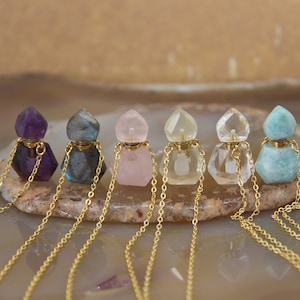 Pode incluir: Seis colares com frasco de perfume de cristal de diferentes pedras preciosas e correntes douradas. Os frascos são de várias cores, incluindo ametista, labradorita, quartzo rosa, quartzo transparente e água-marinha.