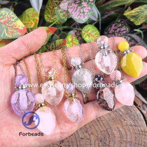 Op de afbeelding: Een verzameling edelsteen hangerkettingen in verschillende kleuren, waaronder paars, helder, roze en geel. Elke ketting heeft een facetgeslepen, druppelvormige hanger met een bijpassende edelsteen stopper en een fijne ketting. De Etsy shopnaam "Forbeads" is zichtbaar.