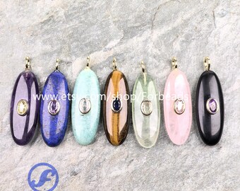 May include: Seven oval-shaped gemstone pendants in various colors, including purple, blue, turquoise, brown, green, pink, and black. Each pendant has a gold-colored bail and a small, round gemstone in the center. The pendants are displayed on a textured gray surface.