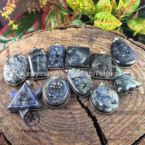 May include: A collection of carved labradorite pendants in various shapes, including oval, rectangular, and star-shaped designs. The pendants feature intricate carvings and silver-colored metal accents. The labradorite stones display blue and gray hues.