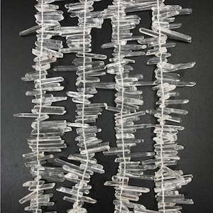 May include: A strand of clear quartz crystal points, also known as rock crystal, arranged in a staggered pattern. The points are various lengths and are strung on a white thread.