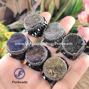 May include: Six rings featuring circular druzy stones in various colors including blue, black, gray, and gold. Each stone is surrounded by a border of small clear crystals set on a dark metal band. The text www.etsy.com/shop/Forbeads is visible.