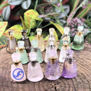 Puede incluir: Una colección de pequeños frascos de perfume decorativos en varios colores, incluyendo transparente, verde, amarillo y morado. Cada frasco tiene un tapón único con forma de cristal y un cuello dorado o plateado. Los frascos están dispuestos sobre una superficie de madera.