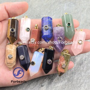 May include: A collection of twelve hexagonal gemstone pendants in various colors including tiger eye, rose quartz, lapis lazuli, amethyst, and black obsidian. Each pendant features a gold-tone bail with a small embedded circular stone.