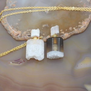 May include: Two agate stone perfume bottle pendants on a gold chain. One bottle is white and the other is gray with a white band.
