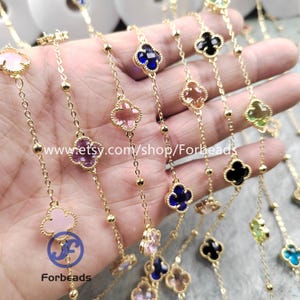 May include: Gold-tone chain necklaces featuring clover-shaped pendants in shades of pink, blue, and black. The necklaces are adorned with small, round beads. The Etsy shop name "Forbeads" is visible in the image.