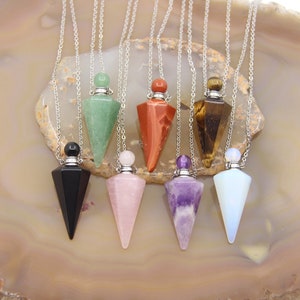 May include: Seven crystal point pendant necklaces with silver chains. The pendants are in the shapes of bottles with stoppers. The crystals are green, red, brown, black, pink, purple, and white.