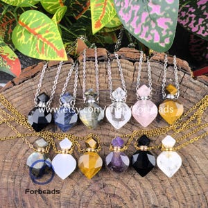 Puede incluir: Surtido de collares con colgantes de piedras preciosas con cadenas de plata. Los colgantes son de varios colores, incluyendo negro, azul, transparente, rosa y amarillo. Los collares se exhiben sobre una superficie de madera. El texto "Forbeads" es visible.