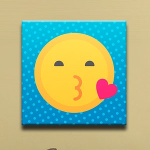 May include: A blue canvas print with white polka dots featuring a yellow emoji face blowing a kiss with a pink heart.