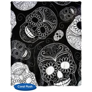 May include: Black and white patterned throw blanket with a repeating design of sugar skulls. The skulls are intricately detailed with floral patterns and swirls.