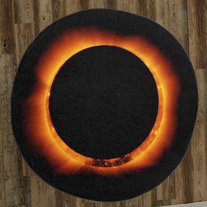 May include: A black and orange round rug with a large, bright orange ring in the center, resembling a solar eclipse.