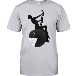 May include: A black and white graphic t-shirt featuring a silhouette of a person hanging from a chain attached to a Pac-Man character.