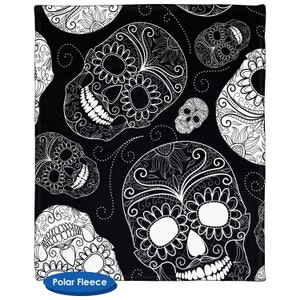 May include: Black and white patterned fleece blanket with a repeating design of sugar skulls. The skulls are intricately detailed with floral patterns and swirls.
