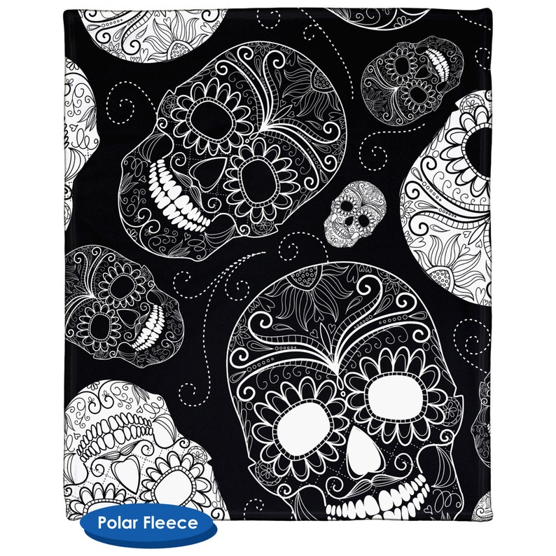 May include: Black and white patterned fleece blanket with a repeating design of sugar skulls. The skulls are intricately detailed with floral patterns and swirls.