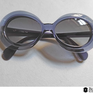 May include: A pair of dark purple oval-shaped sunglasses with a thin black frame.