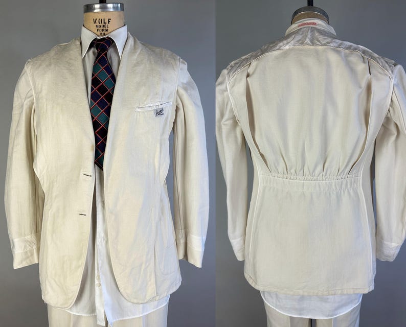 May include: An off-white blazer featuring a two-button front closure, a chest pocket with a small label, and long sleeves. The back displays a gathered waist detail with a horizontal seam. A white collared shirt and a dark tie with a grid pattern.