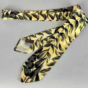 May include: A yellow silk tie with a black and green leaf pattern. The tie has a brown label that reads "Debron's, Hand Made Neckwear, New York".