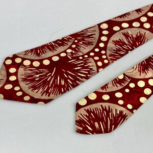 May include: A red tie with a repeating pattern of beige circles and white dots. The tie has a shiny finish and a classic shape. The design features a radial pattern with a vintage aesthetic.