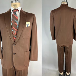 May include: A brown suit displayed on a mannequin. The suit includes a two-button jacket with a notched lapel, a pocket square, and matching trousers. A patterned tie with red and blue accents adds a pop of color. The suit is a classic style.