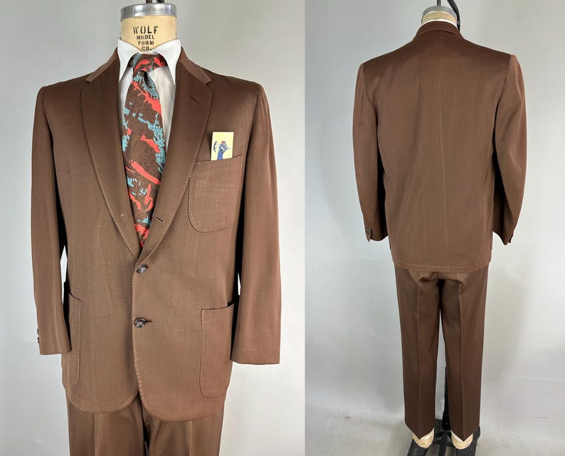 May include: A brown suit displayed on a mannequin. The suit includes a two-button jacket with a notched lapel, a pocket square, and matching trousers. A patterned tie with red and blue accents adds a pop of color. The suit is a classic style.