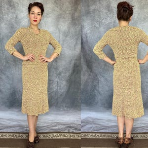 May include: A vintage two-piece dress set in a speckled pattern of tan and red. The set includes a long-sleeved top with a V-neck and a knee-length skirt. The outfit is worn by a person in a studio setting.