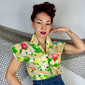 May include: Tan short-sleeved button-up shirt with a tropical floral and cocktail print. The shirt features a collared neckline and is adorned with green, yellow, red, and white floral and cocktail designs. The shirt is made of a lightweight fabric.