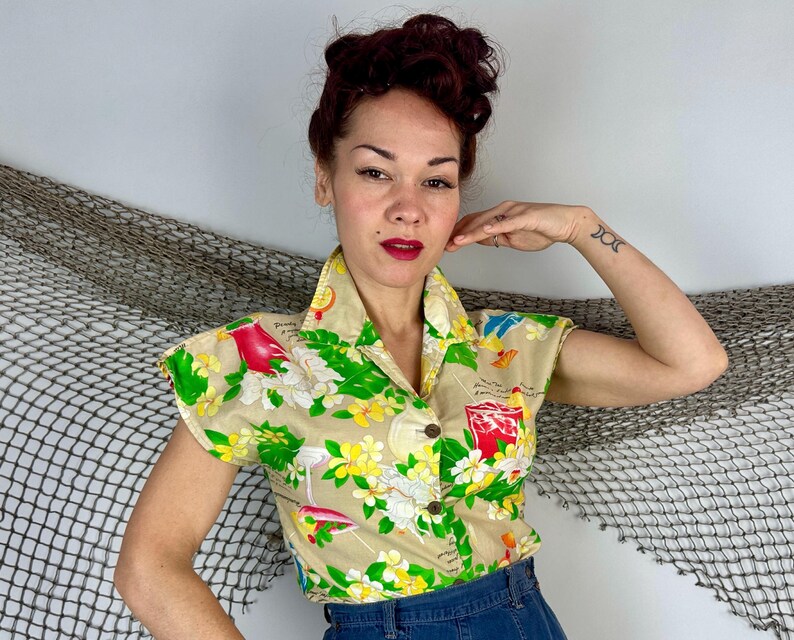 May include: Tan short-sleeved button-up shirt with a tropical floral and cocktail print. The shirt features a collared neckline and is adorned with green, yellow, red, and white floral and cocktail designs. The shirt is made of a lightweight fabric.