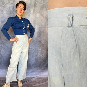 May include: A royal blue long-sleeve cropped cardigan with white buttons and a letter patch, paired with high-waisted light blue trousers featuring a single white button closure, belt loops, and vertical pleats at the front waistline.
