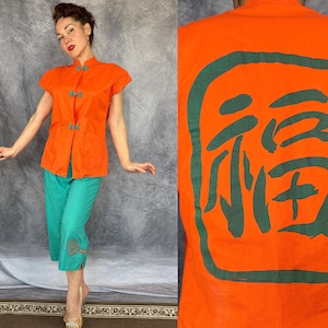 May include: An orange short-sleeved top with frog closures and teal capri pants. The pants have embroidered details at the hem. The back of the top features a large green Chinese character.