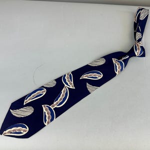 May include: A navy blue tie with a repeating pattern of white, tan, and blue paisley shapes and striped ovals. The tie is knotted at the top, showcasing the design. The tie is a classic accessory.