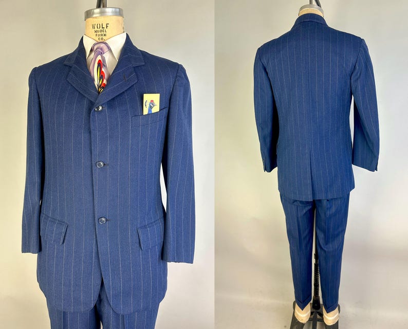 Puede incluir: Un traje azul de rayas diplom&aacute;ticas que incluye una chaqueta de tres botones con solapas de muesca, dos bolsillos con solapa y un bolsillo en el pecho con una tarjeta amarilla que muestra la ilustraci&oacute;n de un p&aacute;jaro azul. Visto de frente y de espaldas.