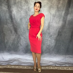 May include: A solid bright red knee-length dress featuring short sleeves, a round neckline, and a fitted bodice with subtle waist pleating details. The garment has a straight skirt silhouette and a clean, simple design without any visible patterns.