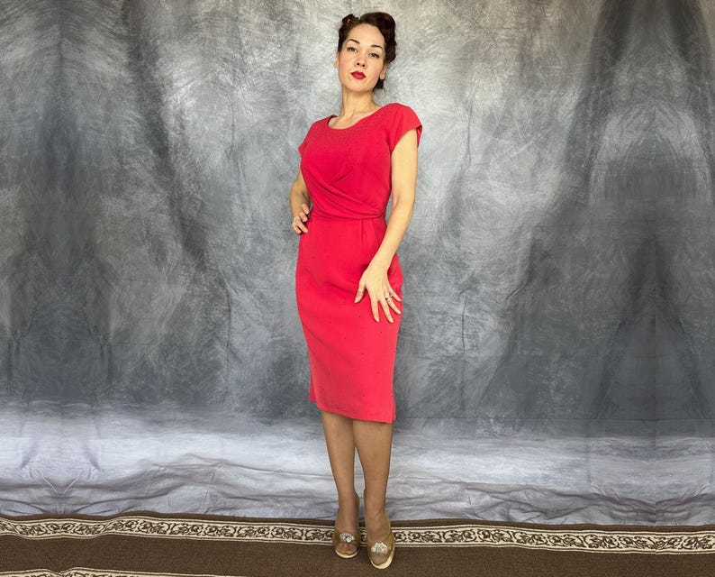 May include: A solid bright red knee-length dress featuring short sleeves, a round neckline, and a fitted bodice with subtle waist pleating details. The garment has a straight skirt silhouette and a clean, simple design without any visible patterns.