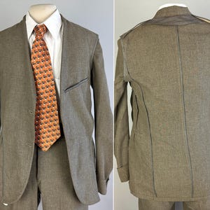 Op de afbeelding: Een taupekleurige blazer met zichtbare naden, gedragen over een wit overhemd met kraag en een oranje stropdas met een herhalend patroon van kleine zwart-witte bloemen. De blazer heeft een revers, twee knopen aan de voorzijde en een borstzak.