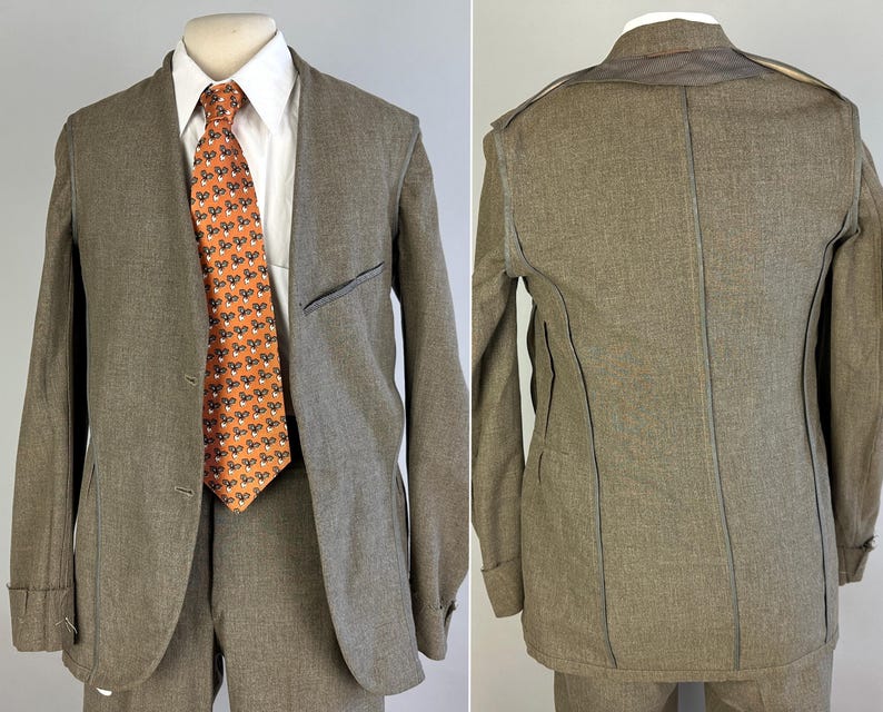 Op de afbeelding: Een taupekleurige blazer met zichtbare naden, gedragen over een wit overhemd met kraag en een oranje stropdas met een herhalend patroon van kleine zwart-witte bloemen. De blazer heeft een revers, twee knopen aan de voorzijde en een borstzak.