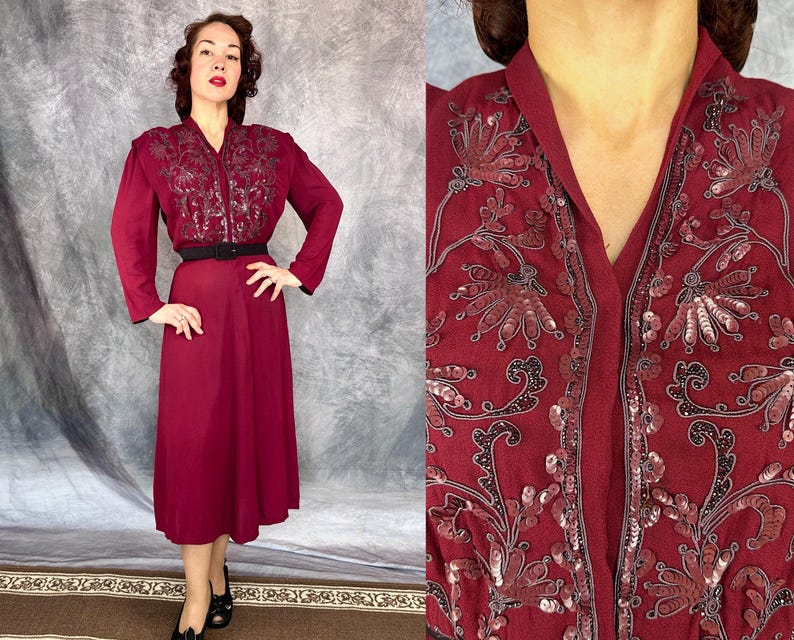May include: A burgundy vintage dress with long sleeves and a V-neckline. The bodice features intricate sequin and embroidered detailing. A black belt cinches the waist, and the dress falls to a midi length. The dress is paired with black shoes.