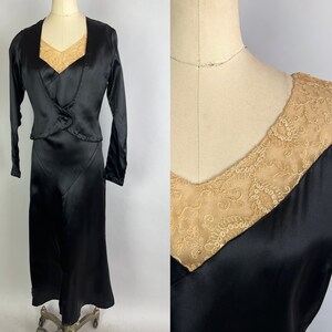 May include: A black satin dress with a matching jacket. The dress has a V-neckline and a lace overlay. The jacket has a shawl collar and long sleeves.