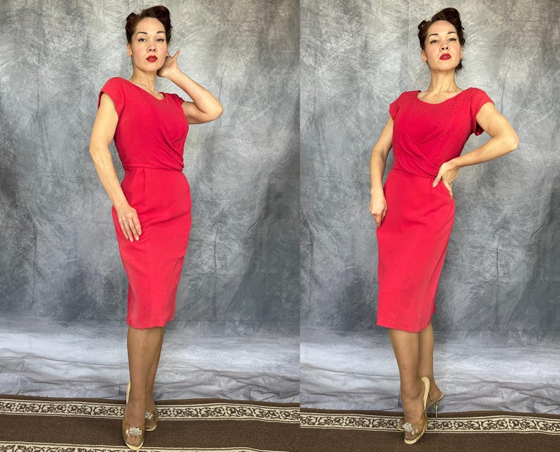 May include: A bright red knee-length dress featuring short sleeves, a round neckline, and a fitted bodice that transitions into a straight skirt. The garment has a solid color finish with subtle draping at the waistline and a clean, tailored silhouette.