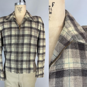 Op de afbeelding: Een vintage geruite jas in bruin-, crème- en grijstinten, met een volledige ritssluiting. De jas heeft een klassieke kraag en lange mouwen. De stof heeft een subtiele textuur en het ruitpatroon is gelijkmatig verdeeld.