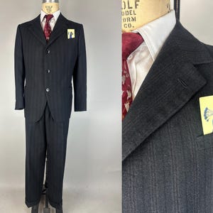 Może przedstawiać: Czarny garnitur w drobną kratę z trzyguzikową marynarką i poszetką z ilustracją pawia. Garnitur ma klasyczny, dopasowany krój.