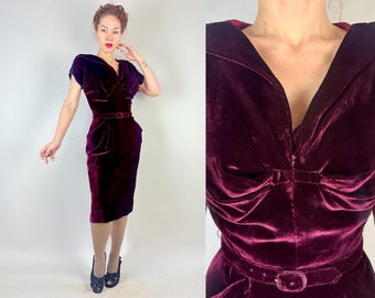 May include: A burgundy velvet dress with a fitted bodice and a full skirt. The dress has a V-neckline and a belt at the waist.