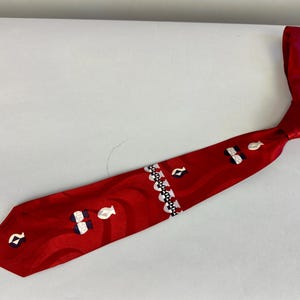 Può includere: Una cravatta di seta rossa con un motivo bianco e blu. Il motivo presenta vasi stilizzati e un motivo geometrico ripetitivo.