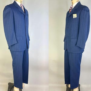 Puede incluir: Un traje azul oscuro con rayas diplom&aacute;ticas que incluye una chaqueta de tres botones con solapas de muesca y pantalones a juego. La chaqueta cuenta con un bolsillo en el pecho con una etiqueta rectangular, dos bolsillos con solapa, camisa y corbata.
