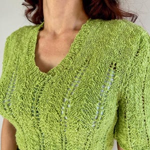 May include: A lime green knit top with a V-neck and short sleeves. The top features a textured, open-weave design with a subtle chevron pattern. The fabric appears soft and lightweight, suitable for warmer weather. The top is a solid color.