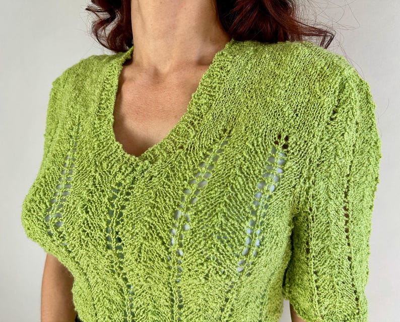 May include: A lime green knit top with a V-neck and short sleeves. The top features a textured, open-weave design with a subtle chevron pattern. The fabric appears soft and lightweight, suitable for warmer weather. The top is a solid color.