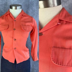 Op de afbeelding: Koraalrood shirt met lange mouwen, twee borstzakken en een knoopsluiting. Het shirt wordt getoond op een mannequin en gecombineerd met een donkerblauwe jeans. Het shirt heeft een klassieke kraag en manchetten met knopen.