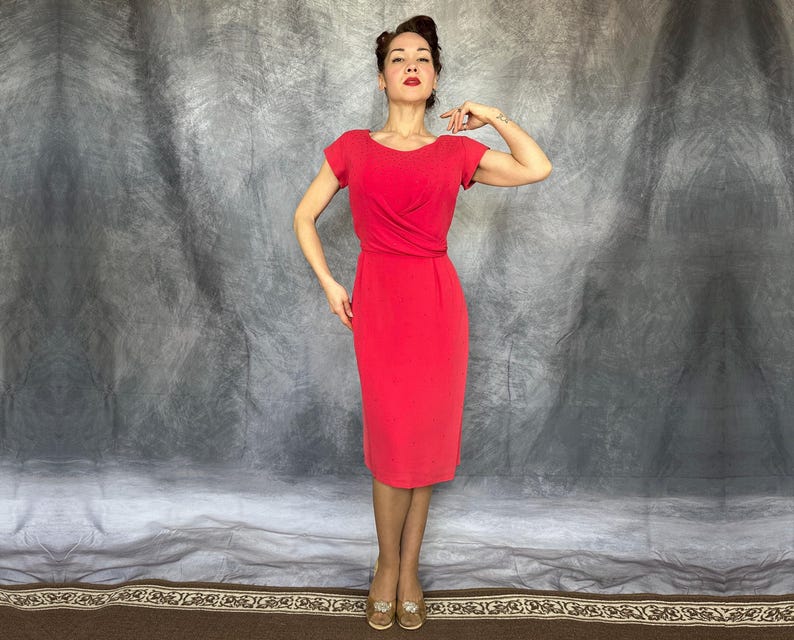 May include: A vibrant red knee-length dress featuring short sleeves, a rounded neckline, and a gathered waist detail. The garment has a fitted silhouette that extends to the knees, showcasing a solid color design with a clean and simple construction.